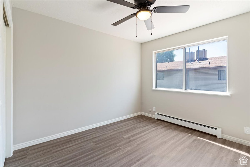 Empty room featuring a baseboard radiator, wood finished floors, baseboards, and ceiling fan