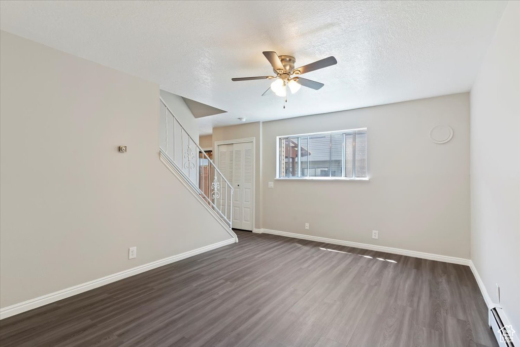 Unfurnished living room featuring a baseboard radiator, dark wood-type flooring, a ceiling fan, baseboards, and a textured ceiling