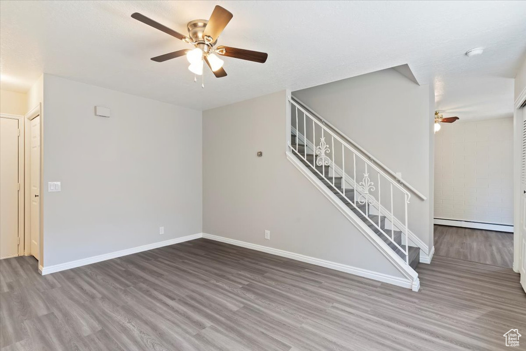 Unfurnished living room with baseboard heating, wood finished floors, a ceiling fan, stairs, and baseboards