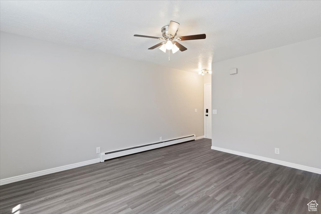 Spare room with baseboard heating, a ceiling fan, dark wood finished floors, and baseboards