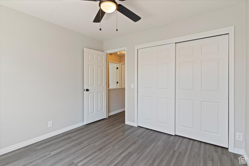 Unfurnished bedroom featuring wood finished floors, baseboards, a closet, and a ceiling fan