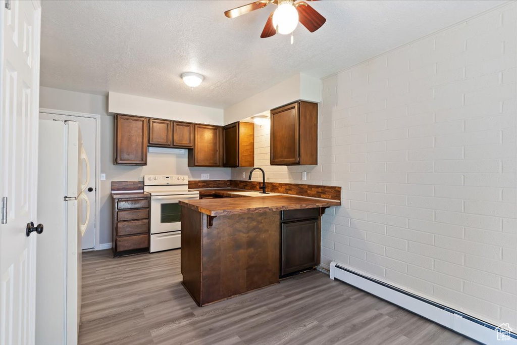 Kitchen featuring white appliances, a baseboard heating unit, a peninsula, a ceiling fan, and wood finished floors