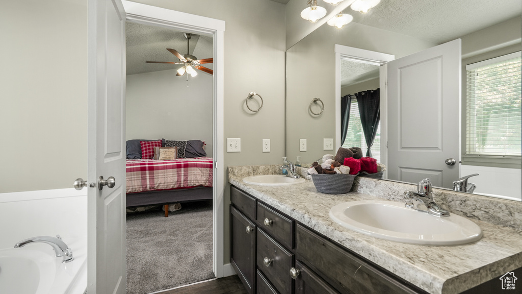 Ensuite bathroom featuring a textured ceiling, double vanity, a ceiling fan, a tub to relax in, and wood finished floors