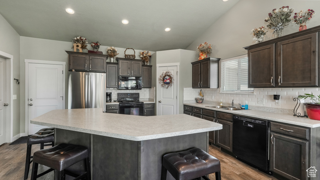 Kitchen featuring black appliances, a breakfast bar area, decorative backsplash, wood finished floors, and a sink
