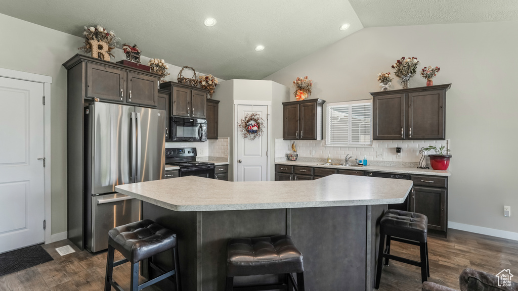 Kitchen featuring black appliances, vaulted ceiling, light countertops, decorative backsplash, and a kitchen bar