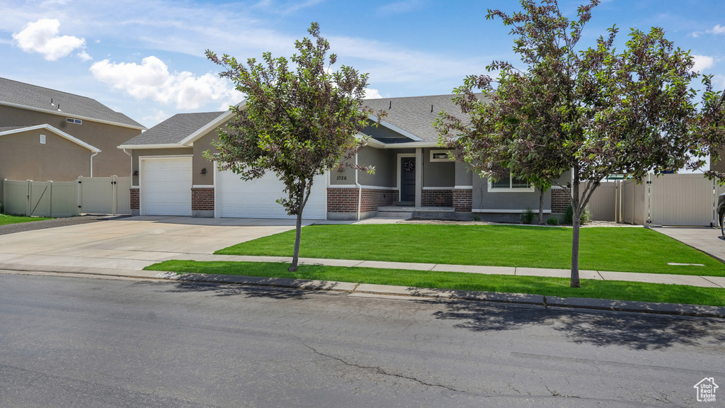 View of property hidden behind natural elements with a gate, a garage, brick siding, and driveway