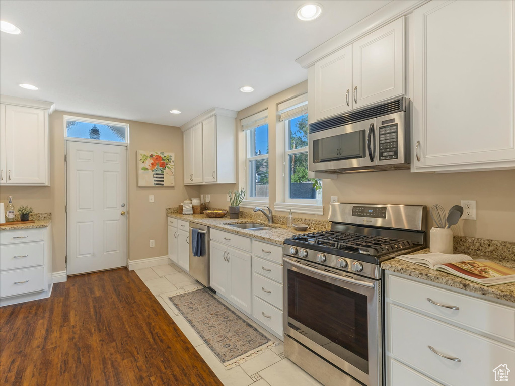 Kitchen with appliances with stainless steel finishes, a sink, white cabinets, recessed lighting, and light stone counters