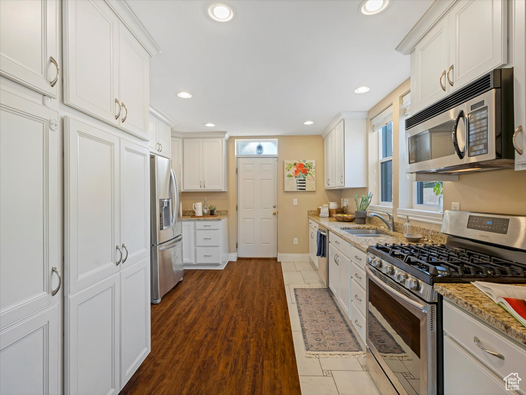 Kitchen with appliances with stainless steel finishes, a sink, white cabinets, baseboards, and recessed lighting