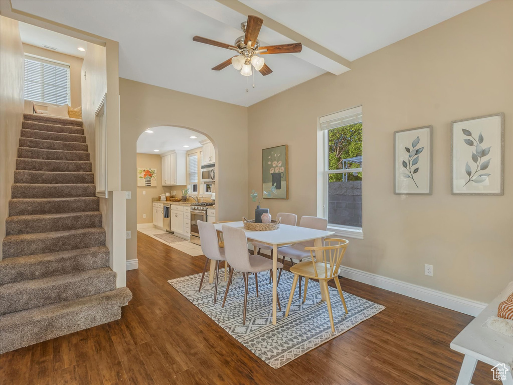 Dining space featuring wood finished floors, arched walkways, a ceiling fan, stairs, and baseboards