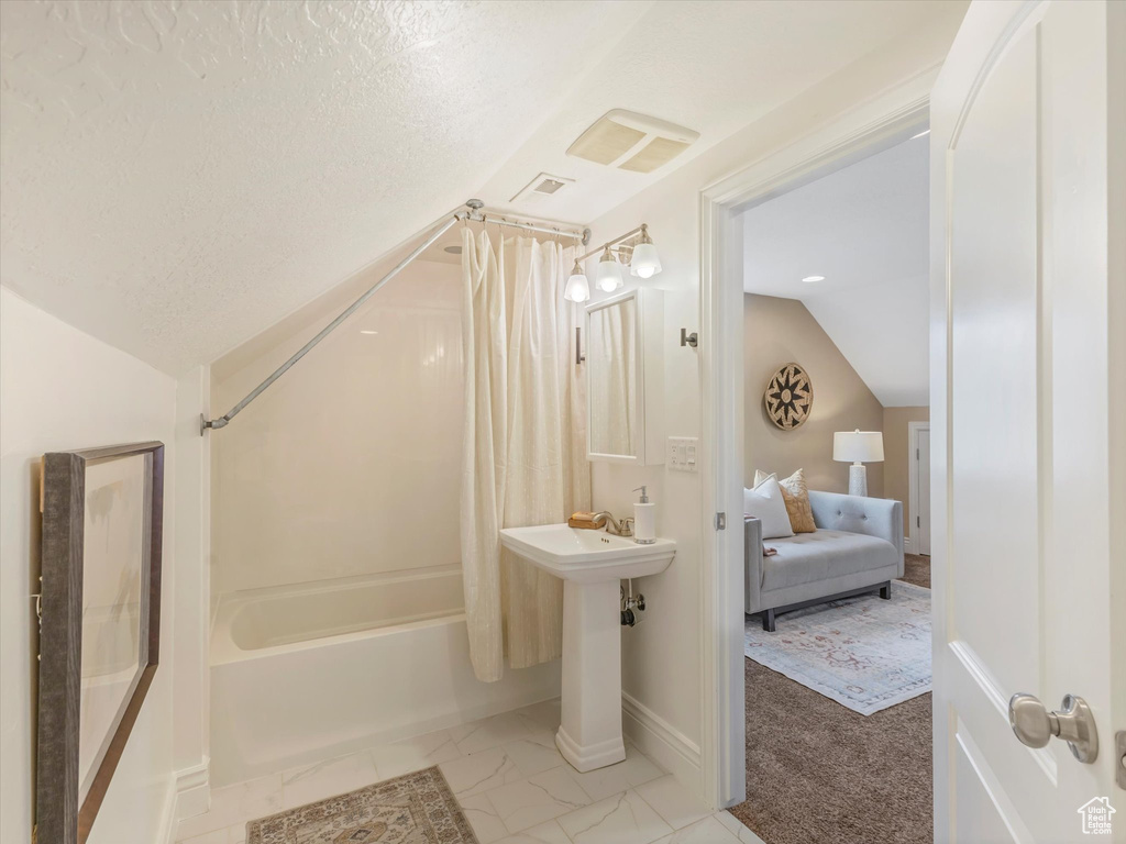 Ensuite bathroom with vaulted ceiling, shower / bath combo with shower curtain, a textured ceiling, baseboards, and a sink