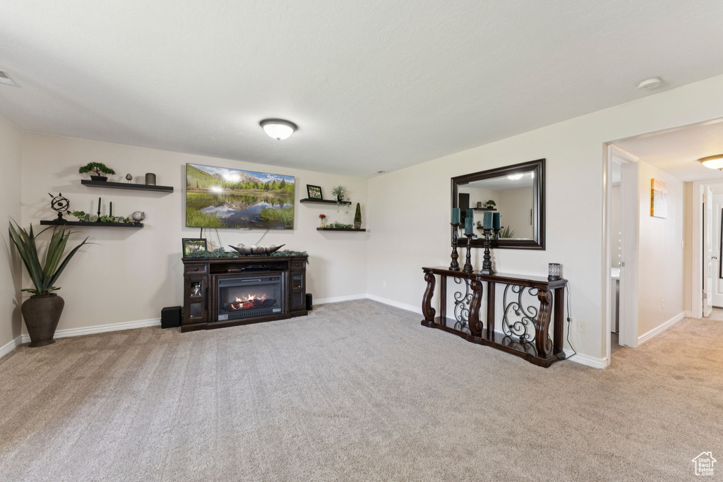 Carpeted living area with a glass covered fireplace and baseboards
