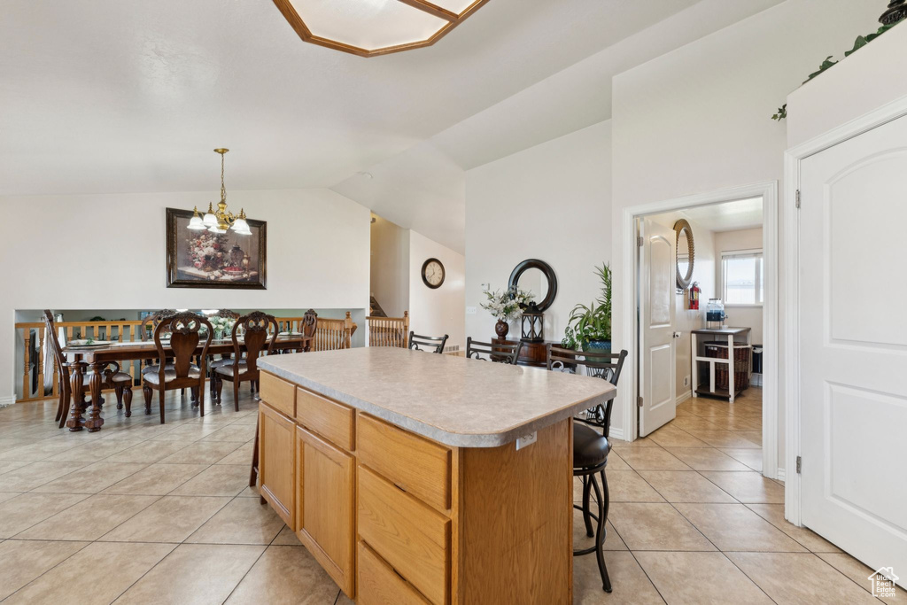 Kitchen featuring a kitchen island, light tile patterned floors, a breakfast bar, vaulted ceiling, and a chandelier