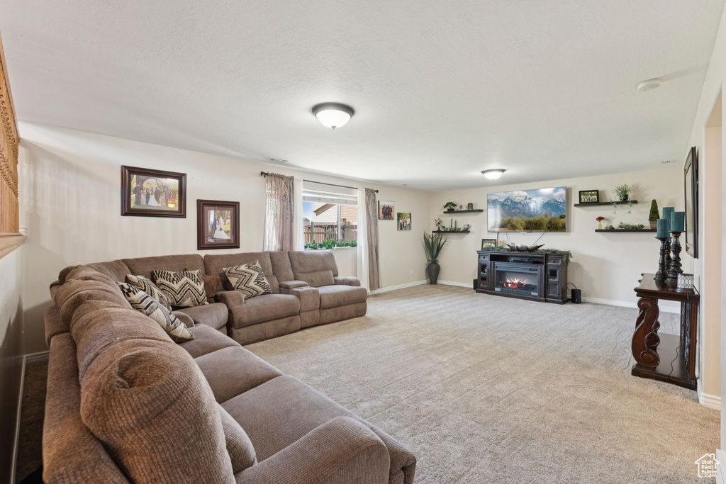 Carpeted living room with a lit fireplace and baseboards