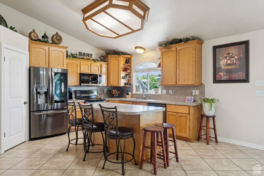 Kitchen featuring stainless steel appliances, lofted ceiling, light tile patterned flooring, tasteful backsplash, and a kitchen bar