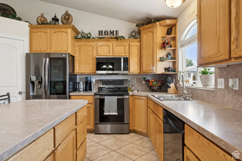 Kitchen featuring stainless steel appliances, a sink, backsplash, light tile patterned flooring, and lofted ceiling