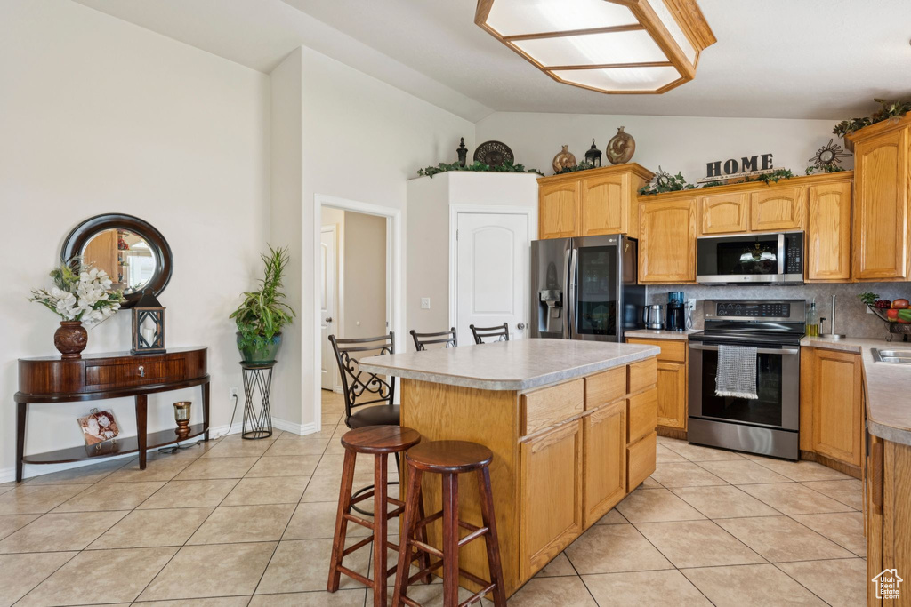 Kitchen featuring appliances with stainless steel finishes, light tile patterned flooring, a kitchen bar, tasteful backsplash, and a center island