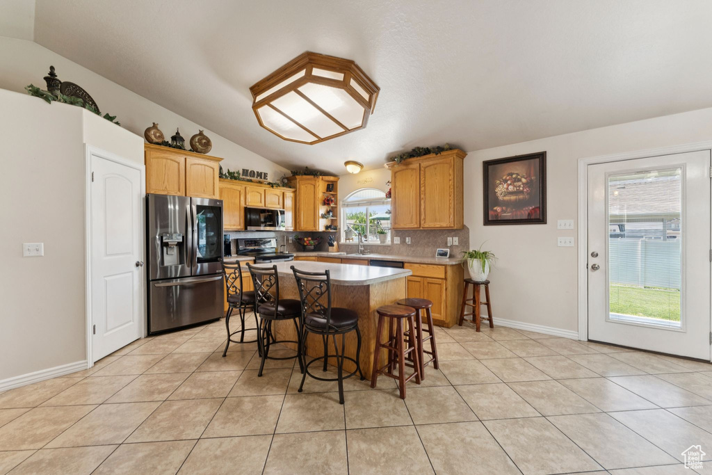 Kitchen featuring stainless steel appliances, vaulted ceiling, backsplash, light tile patterned floors, and a breakfast bar area