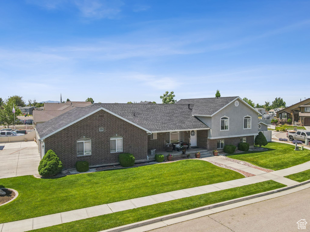 Tri-level home featuring brick siding, concrete driveway, a front yard, and a shingled roof