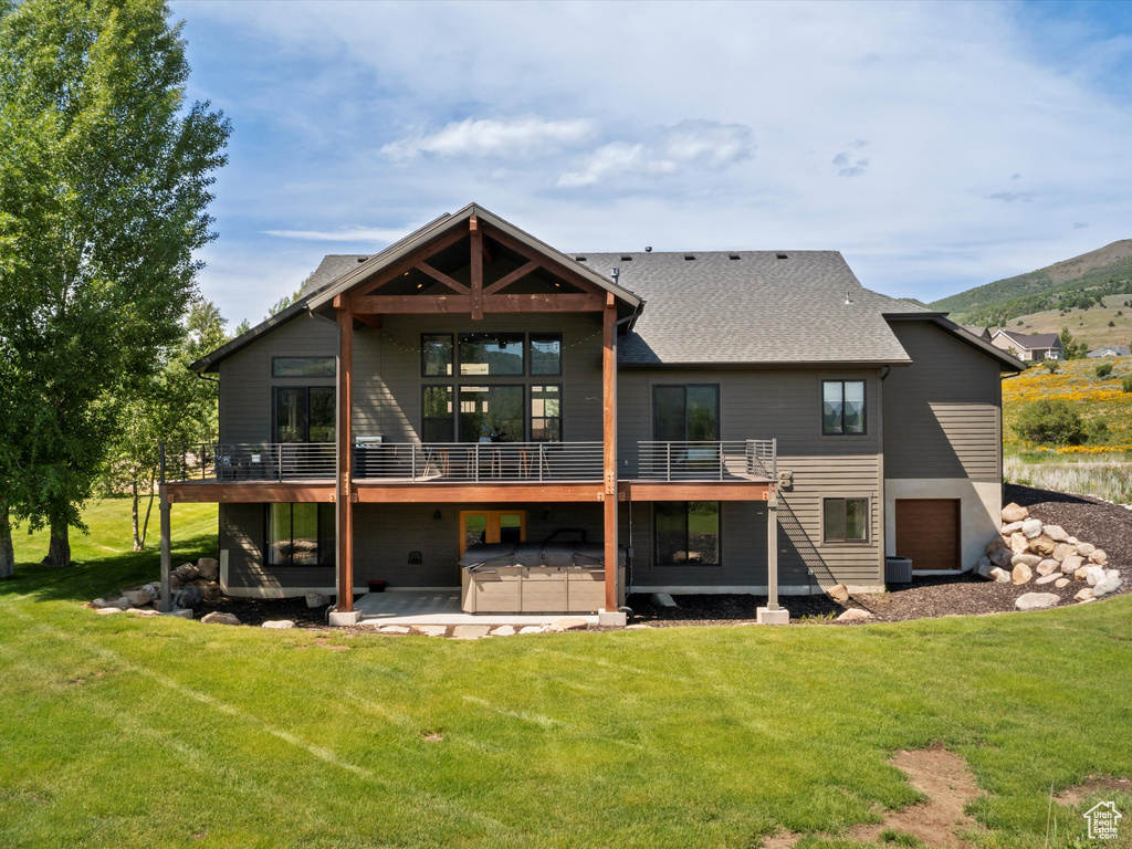 Rear view of property featuring a hot tub, a lawn, a patio area, and an attached garage
