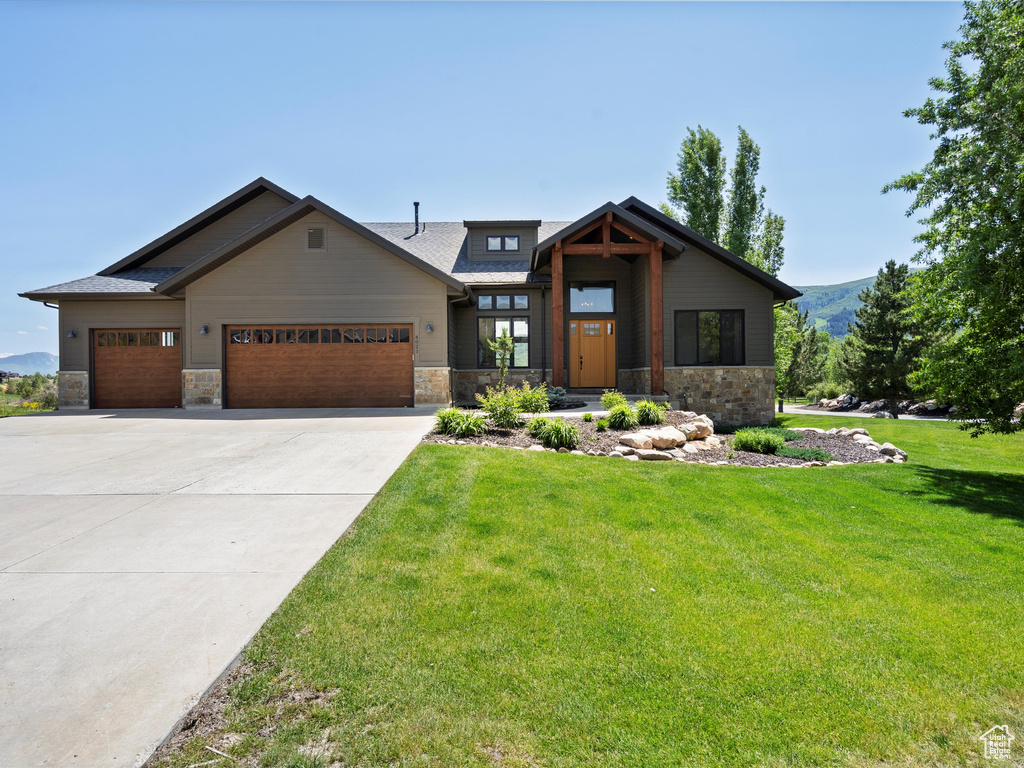 View of front of house featuring stone siding, a garage, and a front lawn