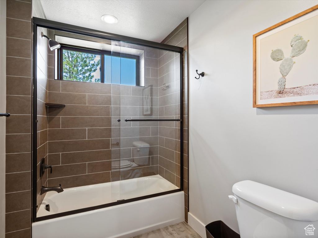 Full bath with toilet, shower / bath combination with glass door, and baseboards