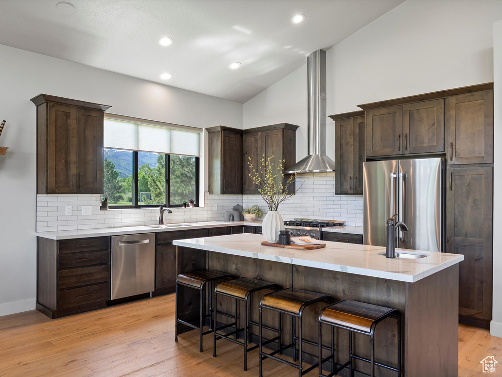 Kitchen with appliances with stainless steel finishes, ventilation hood, a sink, dark brown cabinets, and backsplash