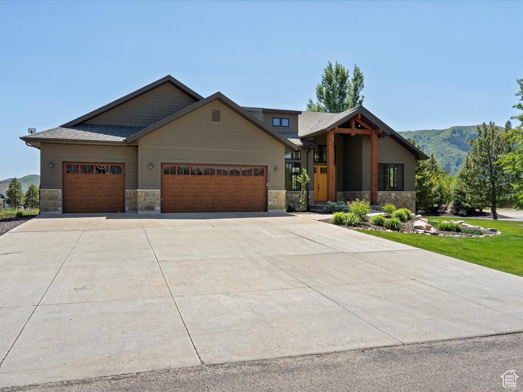 View of front of property with stone siding, an attached garage, concrete driveway, and a mountain view