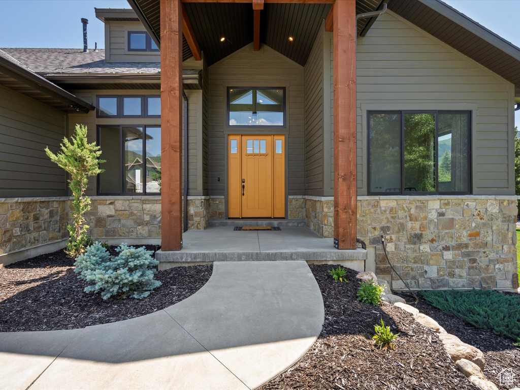 Entrance to property featuring stone siding and roof with shingles