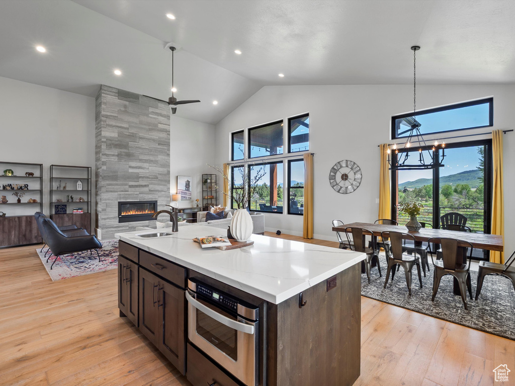 Kitchen with a tile fireplace, stainless steel oven, high vaulted ceiling, light wood-type flooring, and open floor plan