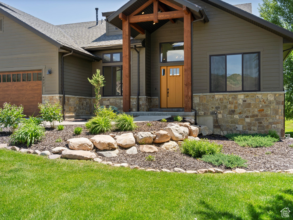 View of front of home with stone siding, roof with shingles, an attached garage, and a front yard
