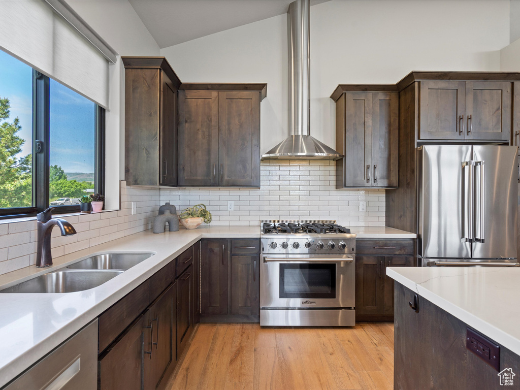 Kitchen featuring premium appliances, wall chimney range hood, a sink, lofted ceiling, and light countertops