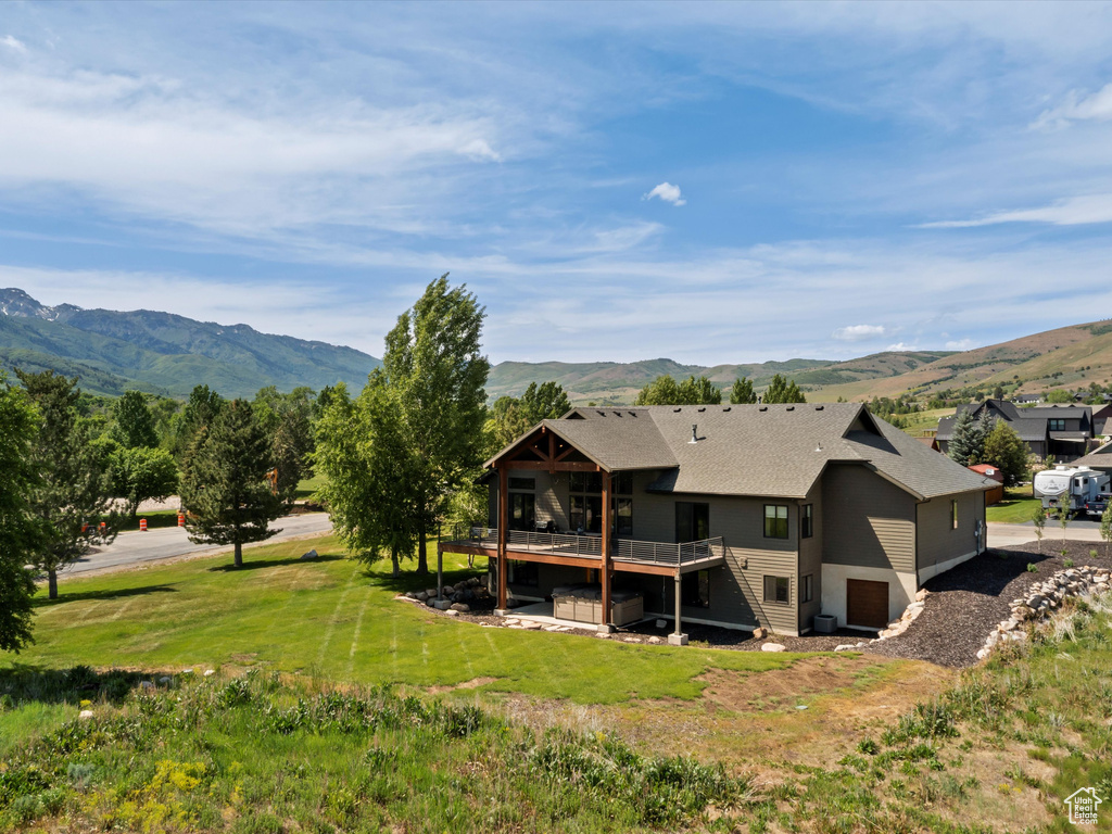 Back of house featuring a deck with mountain view, a shingled roof, and a lawn