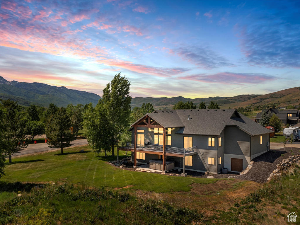 Rear view of house with a deck with mountain view, an attached garage, and a yard
