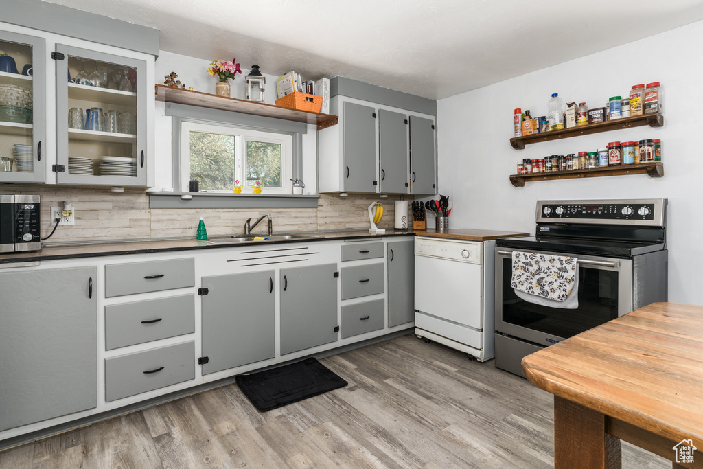 Kitchen featuring appliances with stainless steel finishes, backsplash, light wood-style flooring, and open shelves