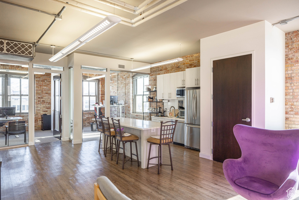 Kitchen with brick wall, appliances with stainless steel finishes, a breakfast bar, a kitchen island, and dark wood finished floors