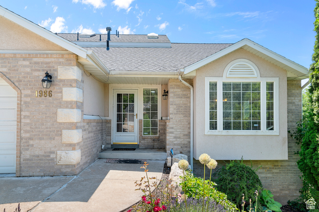Doorway to property featuring roof with shingles, stucco siding, and stone siding