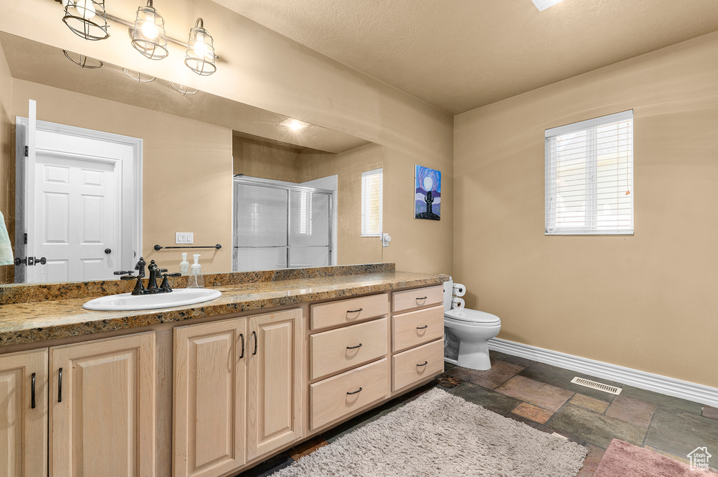 Bathroom featuring a stall shower, vanity, baseboards, stone tile flooring, and toilet
