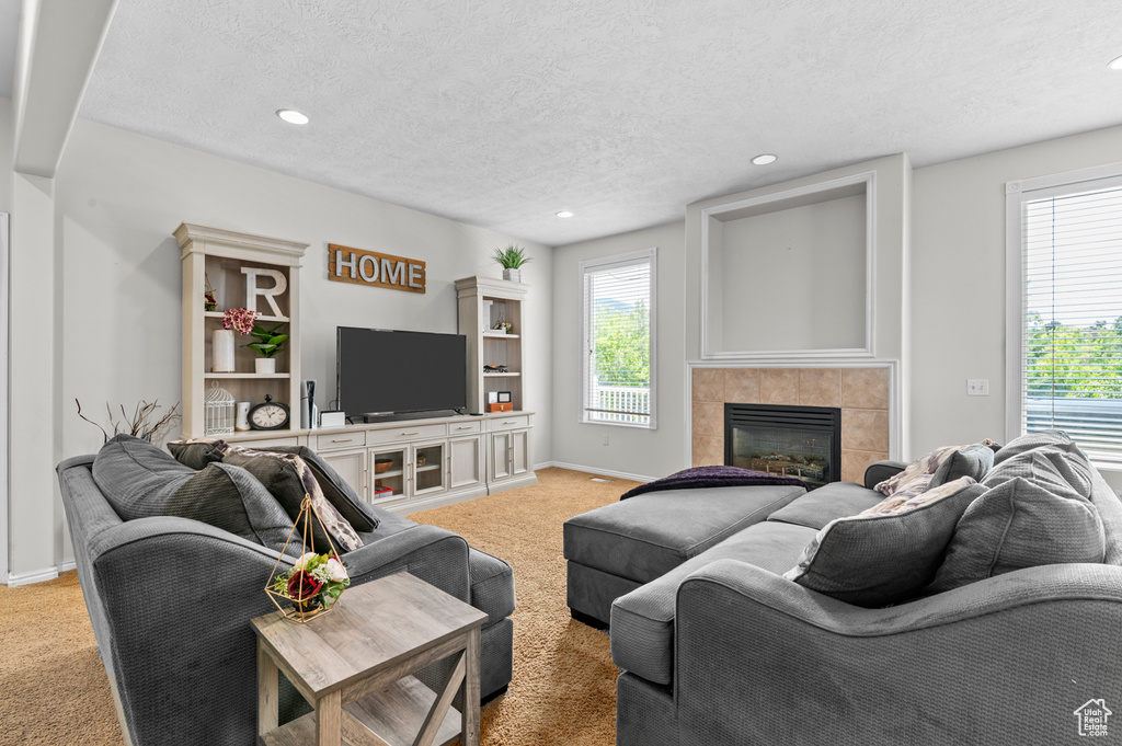 Living room with light carpet, plenty of natural light, a tile fireplace, a textured ceiling, and baseboards