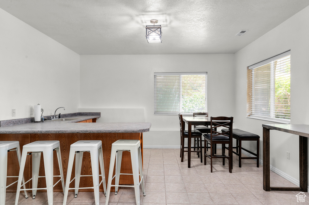 Dining space with a textured ceiling, light tile patterned flooring, and bar with sink