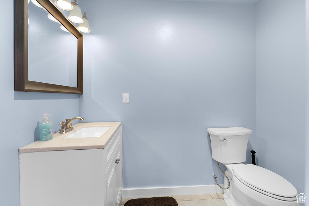 Half bath featuring vanity, toilet, baseboards, and tile patterned floors