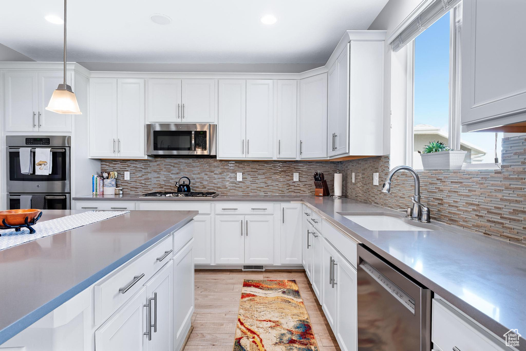 Kitchen with appliances with stainless steel finishes, a sink, light wood-style flooring, white cabinetry, and decorative light fixtures