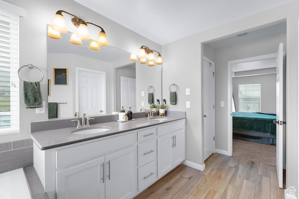 Ensuite bathroom featuring double vanity, wood finished floors, and baseboards