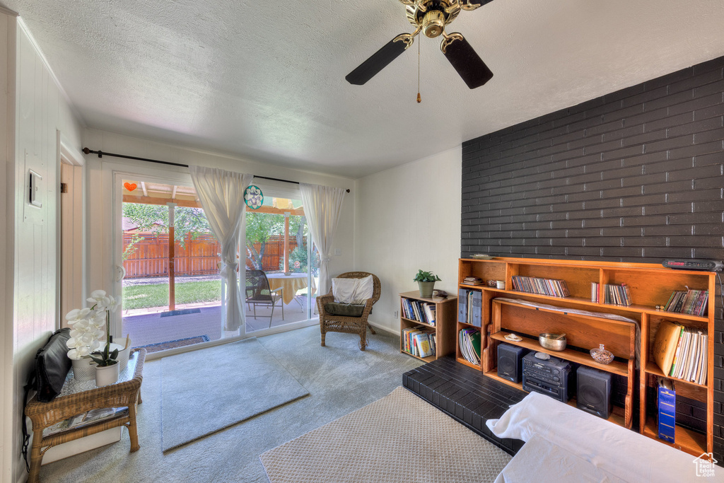 Living area with carpet floors, a textured ceiling, ceiling fan, and brick wall