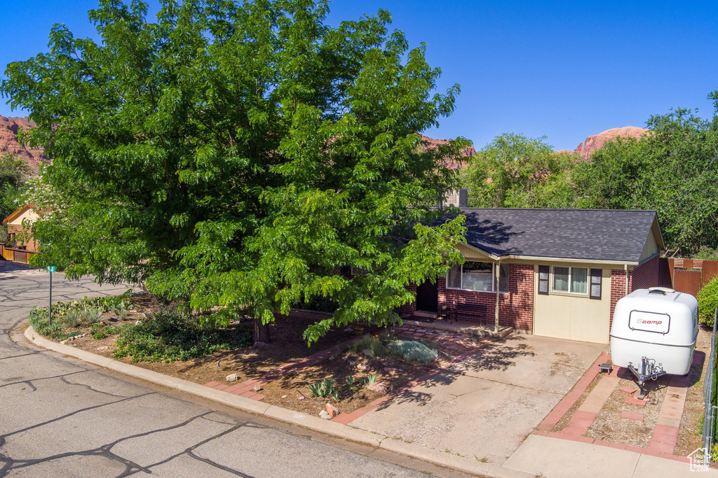 View of property hidden behind natural elements featuring brick siding, a shingled roof, and driveway