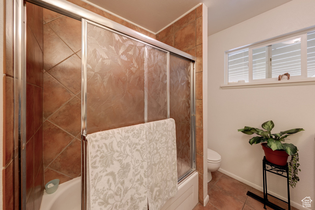 Full bathroom featuring toilet, tile patterned floors, bath / shower combo with glass door, and baseboards