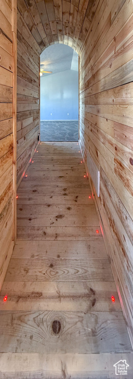 Hall featuring wood walls, wood-type flooring, and vaulted ceiling