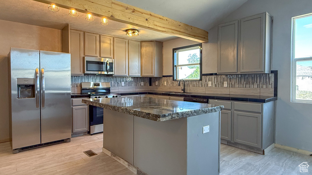 Kitchen featuring stainless steel appliances, a sink, tasteful backsplash, a center island, and beam ceiling