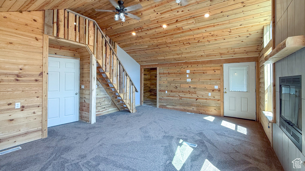 Unfurnished living room featuring wood walls, wood ceiling, a ceiling fan, stairs, and carpet