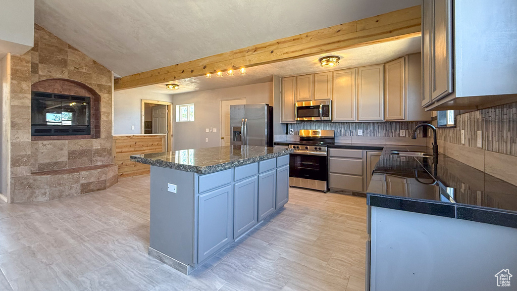Kitchen with stainless steel appliances, a sink, a kitchen island, dark countertops, and backsplash