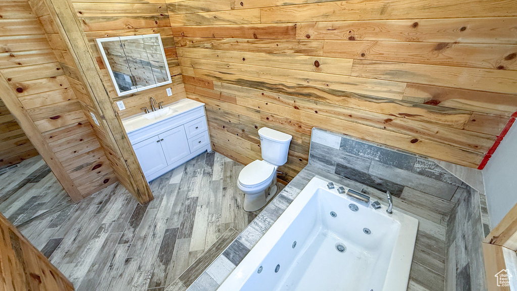 Bathroom with vanity, toilet, a whirlpool tub, wooden walls, and wood finished floors